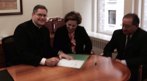 A priest signs a document with two other people