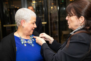 A Woman Putting a pin on Another Woman's Blazer