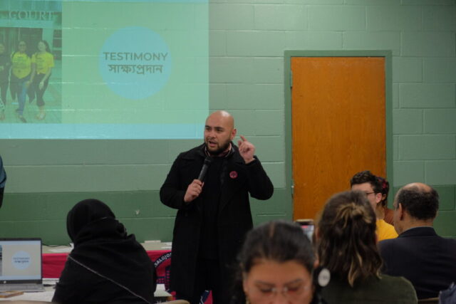 An individual standing in a community room speaking to a crowd of people.